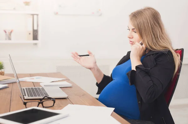 Беременная деловая леди на работе разговаривает по телефону — стоковое фото