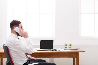 Genç erkek konsantre bu manager gömlekli modern beyaz ofiste bir telefon konuşma vardır.