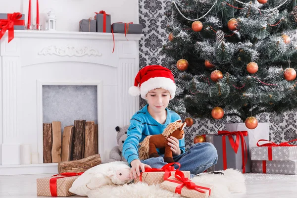 Bonito menino feliz em santa chapéu com presentes de Natal de brinquedo — Fotografia de Stock