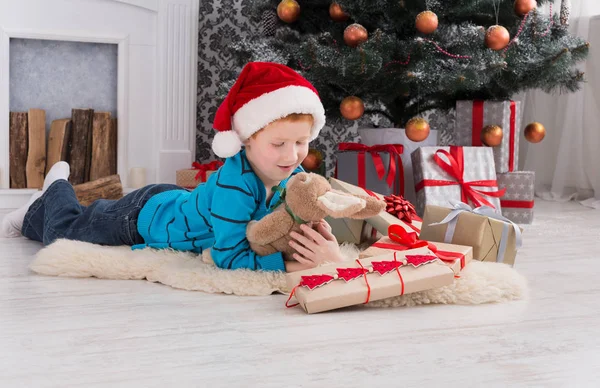 Bonito menino feliz em santa chapéu com presentes de Natal de brinquedo — Fotografia de Stock