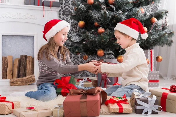 Niños felices en sombreros de Papá Noel desenvolviendo regalos de Navidad —  Fotos de Stock