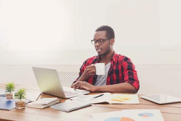 Homme d'affaires noir détendu dans un bureau décontracté, travailler avec un ordinateur portable, boire du café — Photo