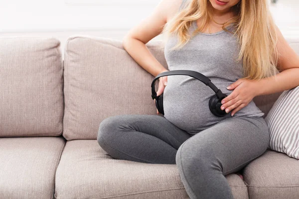 Karnında kulaklık tutan hamile bir kadın.