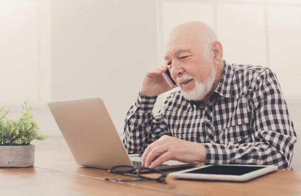 Senior man talking on phone with laptop