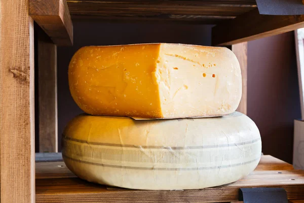 Жесткий сыр как колесо и кусок на полке продуктового магазина крупным планом — стоковое фото