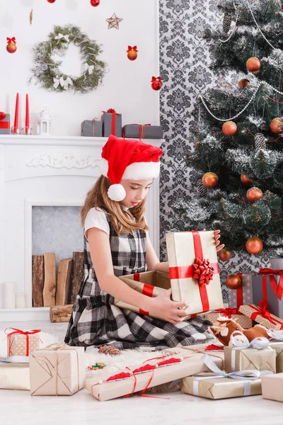 Schönes Mädchen mit Weihnachtsmütze beim Auspacken von Weihnachtsgeschenken — Stockfoto