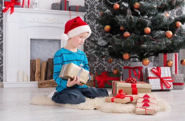 Menino bonito em santa chapéu desembrulhando presentes de Natal — Fotografia de Stock