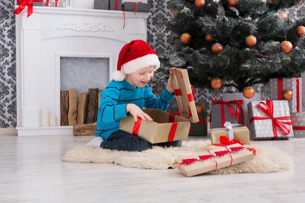 Симпатичний хлопчик у капелюсі Санта, який не завантажує різдвяні подарунки — стокове фото