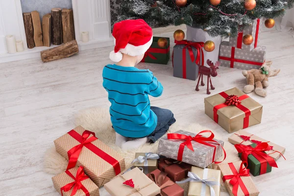 Menino bonito em santa chapéu desembrulhando presentes de Natal — Fotografia de Stock