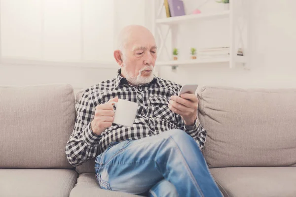 Senior man using smartphone while drinking coffee