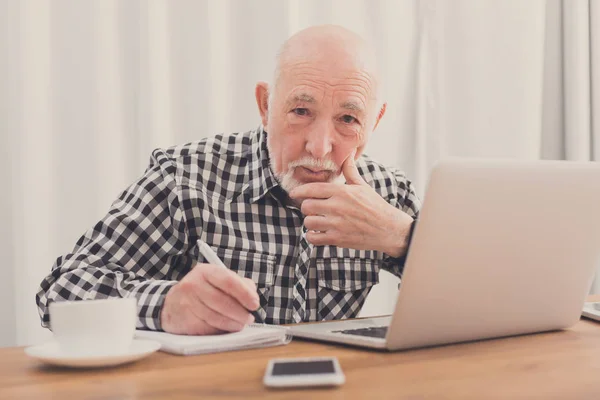 Reifer Mann benutzt Laptop und schreibt in Notizblock — Stockfoto