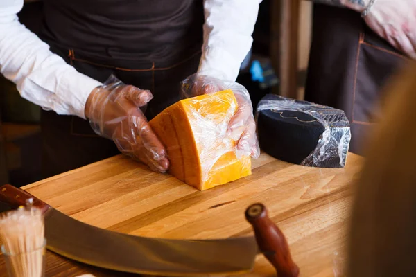 Помощник продавца заворачивает кусок сыра за прилавком — стоковое фото