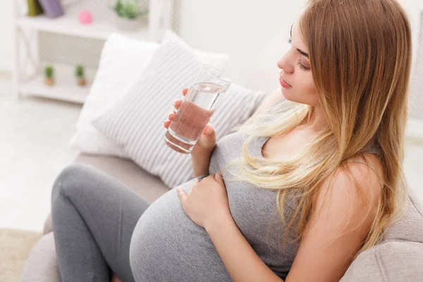 Kobieta w ciąży, popijając szklanką wody, siedząc na kanapie zbliżenie — Zdjęcie stockowe