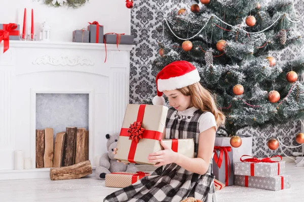 Hermosa chica en santa hat desenvolver regalos de Navidad —  Fotos de Stock