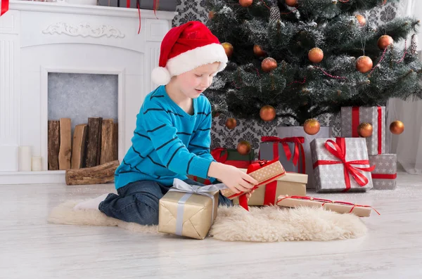 Menino bonito em santa chapéu desembrulhando presentes de Natal — Fotografia de Stock