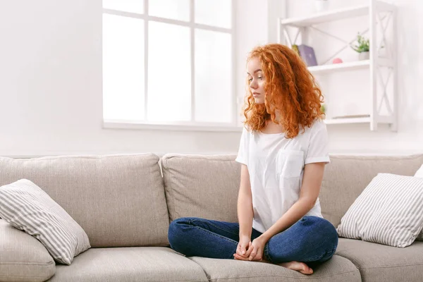 Молодая рыжая женщина думает о бежевом диване — стоковое фото