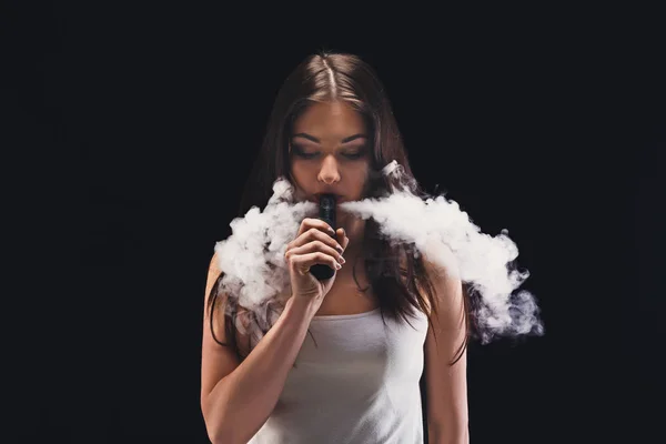 Mujer joven vapeando e-cigarrillo con humo en negro — Foto de Stock