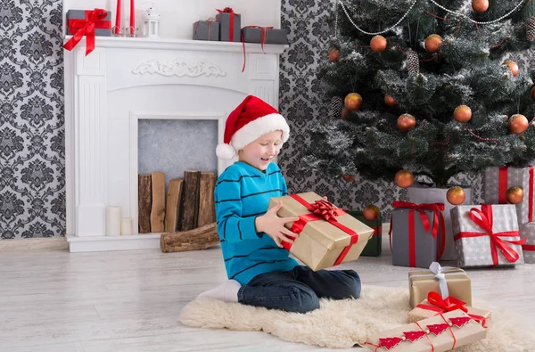 Menino bonito em santa chapéu desembrulhando presentes de Natal — Fotografia de Stock