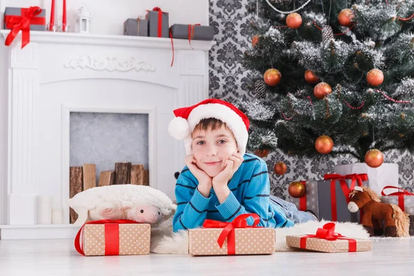 Menino bonito em santa chapéu desembrulhando presentes de Natal — Fotografia de Stock