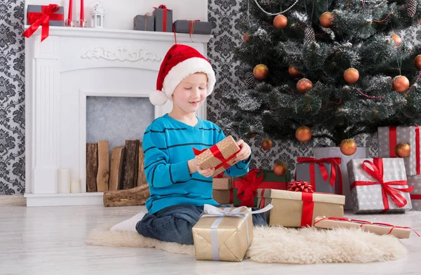 Menino bonito em santa chapéu desembrulhando presentes de Natal — Fotografia de Stock