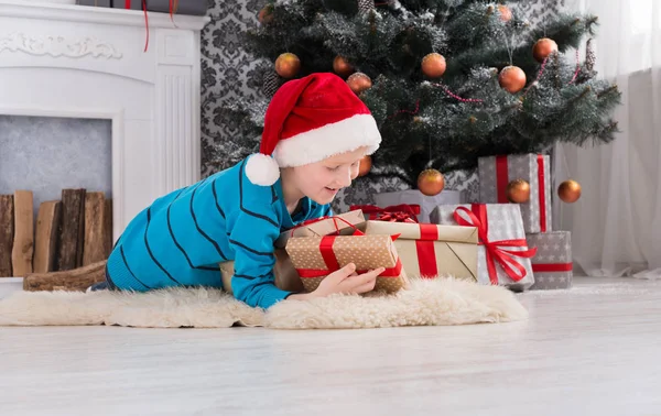 Menino bonito em santa chapéu desembrulhando presentes de Natal — Fotografia de Stock