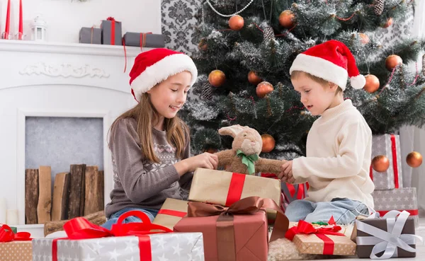 Niños felices en sombreros de Papá Noel desenvolviendo regalos de Navidad —  Fotos de Stock