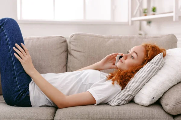 Giovane ragazza parlando sul cellulare sdraiato sul divano beige — Foto Stock