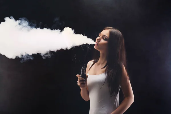 Mujer joven vapeando e-cigarrillo con humo en negro — Foto de Stock