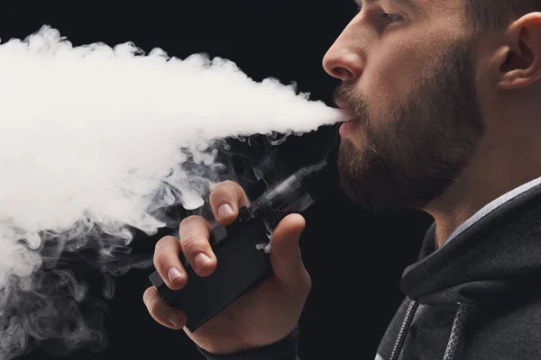 Hombre joven vapeando e-cigarrillo con humo en negro —  Fotos de Stock