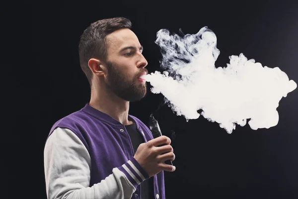 Homem jovem vaping e-cigarro com fumaça em preto — Fotografia de Stock