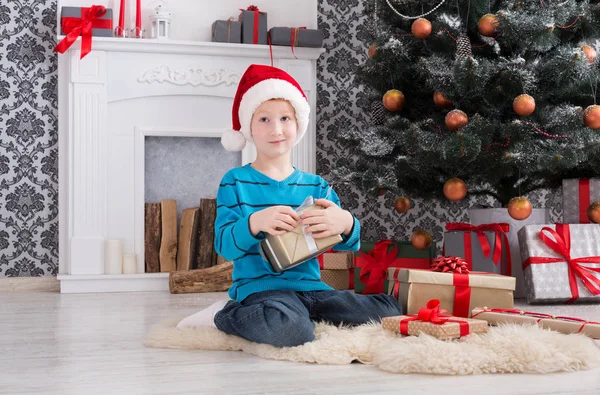 Menino bonito em santa chapéu desembrulhando presentes de Natal — Fotografia de Stock