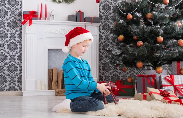 Süßer glücklicher Junge mit Weihnachtsmütze und Spielzeug-Weihnachtsgeschenken — Stockfoto