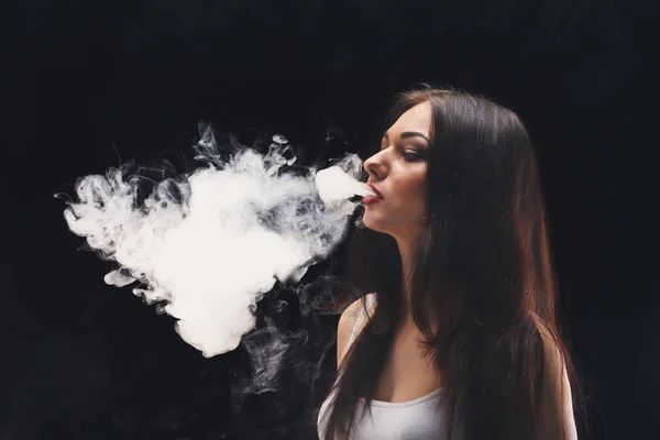 Junge Frau verdampft E-Zigarette mit Rauch auf schwarz — Stockfoto