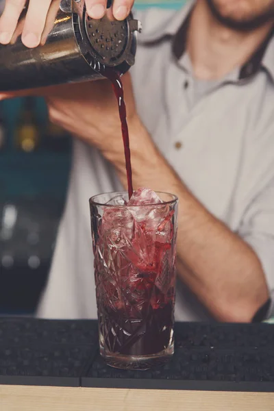 Young bartender pouring cocktail drink into glass