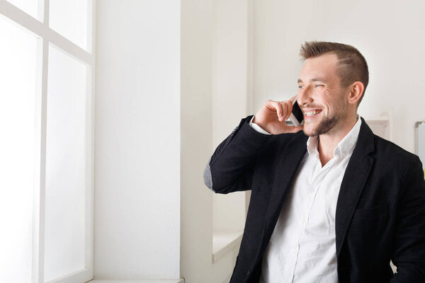 Businessman talking by phone, standing near window