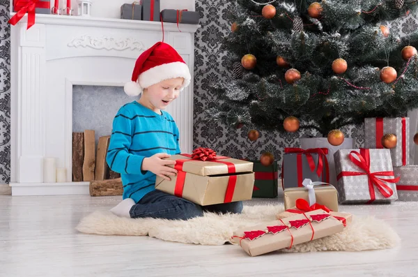 Lindo chico en santa sombrero desenvolver regalos de Navidad —  Fotos de Stock