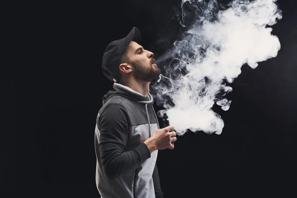 Homem jovem vaping e-cigarro com fumaça em preto — Fotografia de Stock