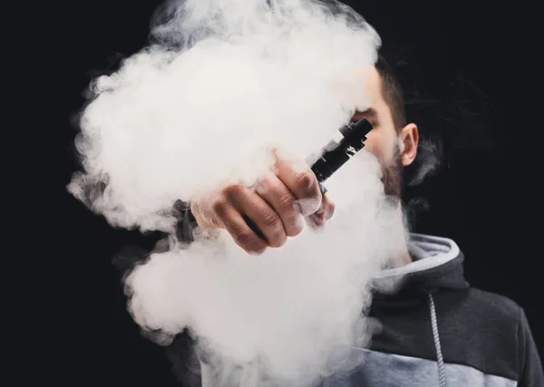 Hombre joven vapeando e-cigarrillo con humo en negro — Foto de Stock