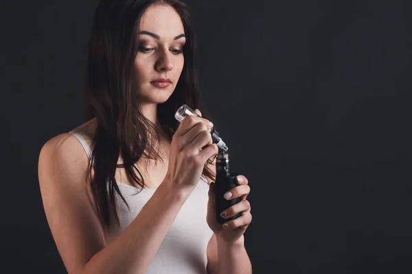 Mujer joven llenando líquido en el cigarrillo electrónico en negro — Foto de Stock