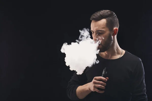 Hombre joven vapeando e-cigarrillo con humo en negro — Foto de Stock