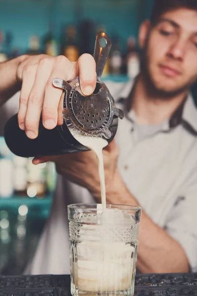 Young bartender pouring cocktail drink into glass