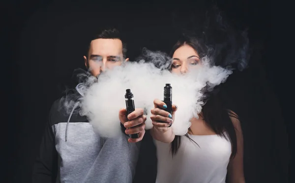 Pareja joven vapeando cigarrillo electrónico con humo en primer plano negro — Foto de Stock