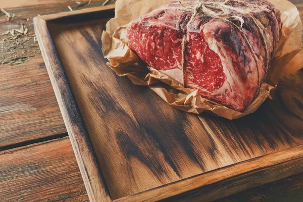 Raw aged prime black angus beef in craft papper on rustic wood — Stock Photo, Image