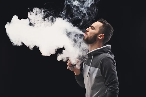 Hombre joven vapeando e-cigarrillo con humo en negro —  Fotos de Stock