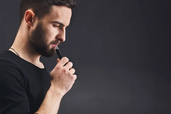 Hombre joven vapeando cigarrillo electrónico en negro —  Fotos de Stock