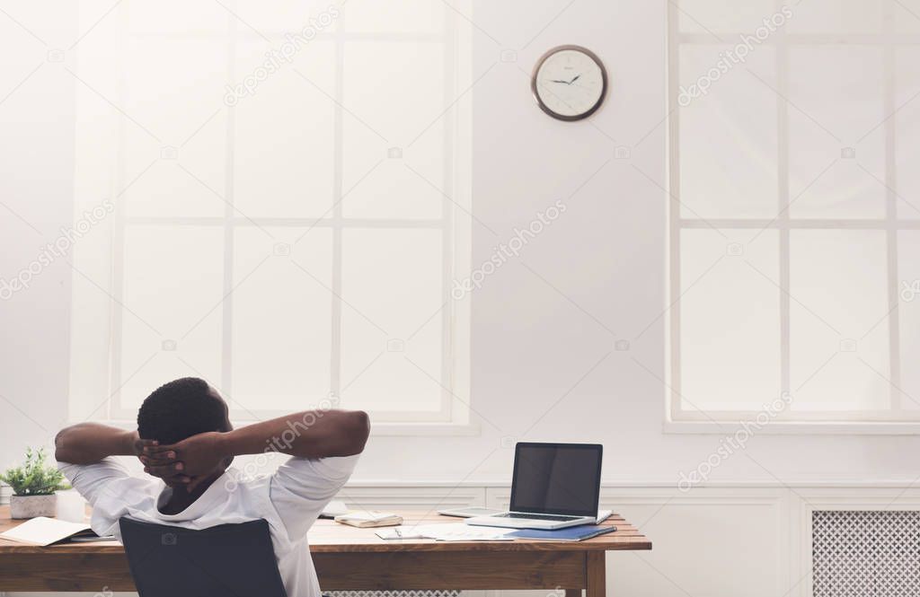 Relaxed black businessman with laptop in modern white office