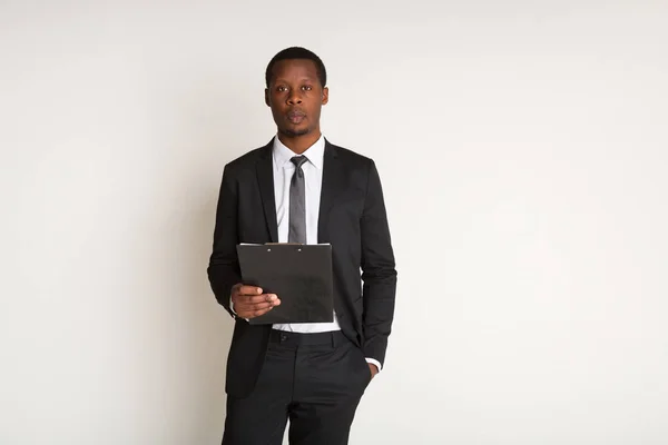 Hombre negro gerente pensativo en traje de pie, la celebración de la computadora portátil. Retrato — Foto de Stock