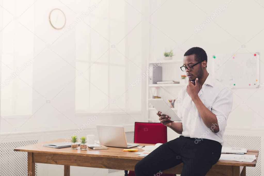 Pensive black businessman in modern office, work with tablet