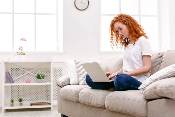 Giovane rossa ragazza con computer portatile seduto sul divano beige — Foto Stock