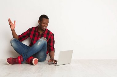 Siyah adam stüdyo katta oturan dizüstü kullanarak gülümseyen